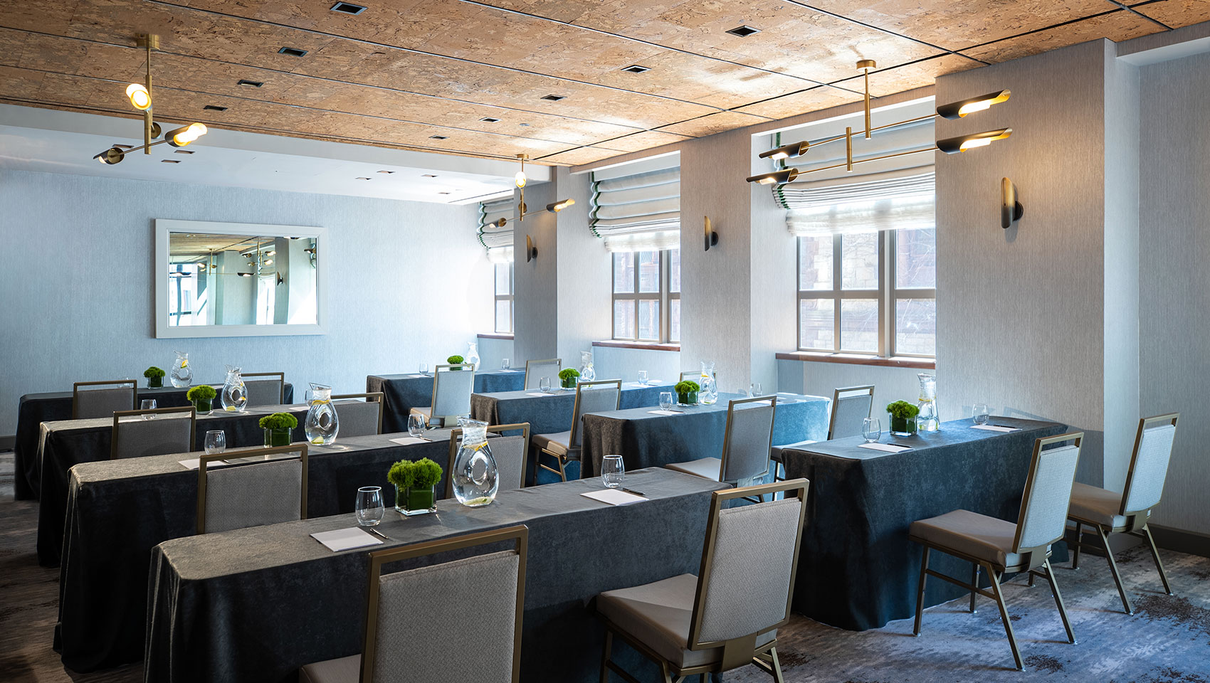 Tyng classroom setup at Kimpton Hotel Palomar Philadelphia showing long tables with notepads on top facing the same direction located next to a wall with large sunlit windows