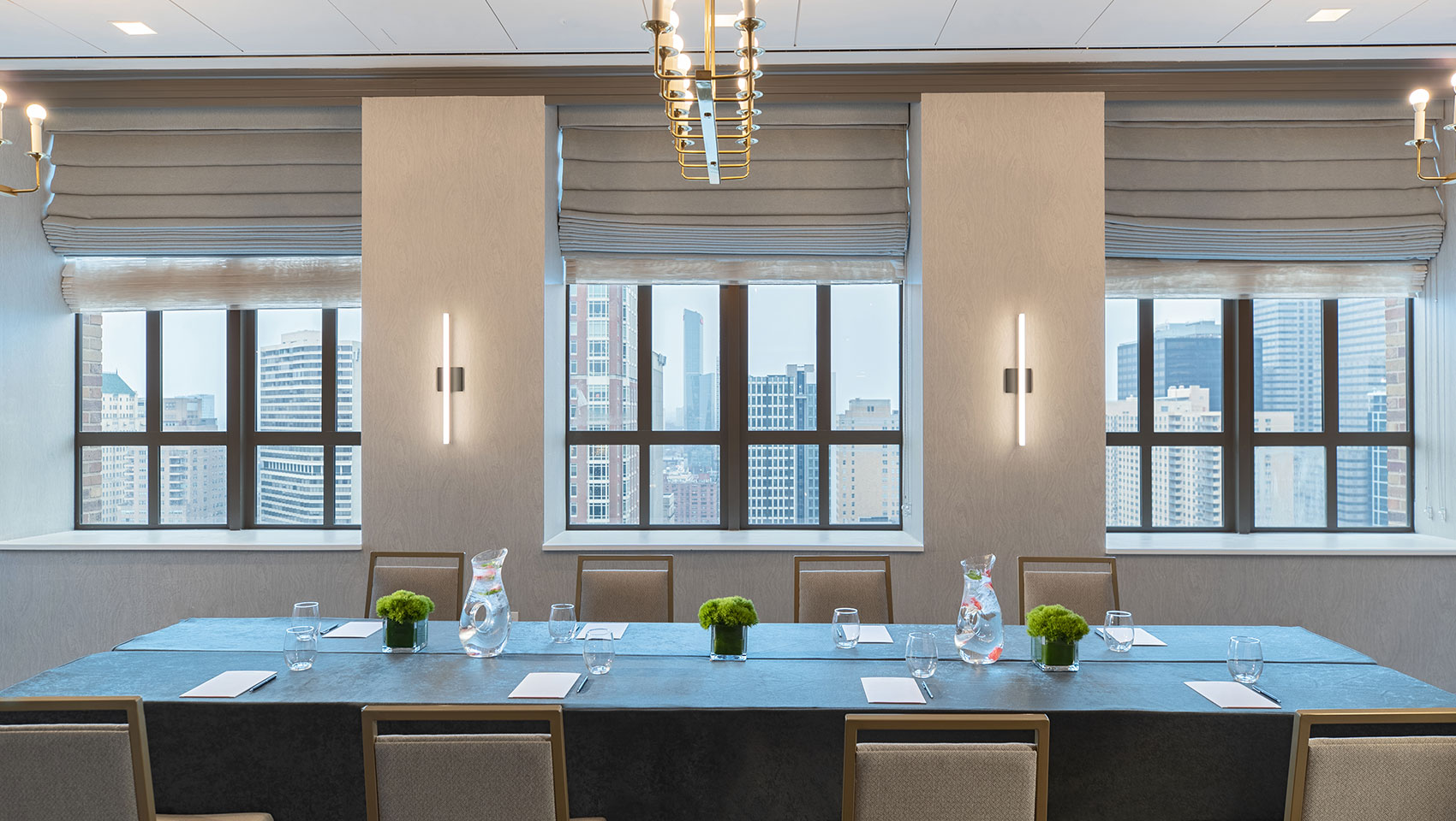 Conference Setup in Abe room located in Kimpton Hotel Palomar Philadelphia showing to long tables with notepads on top surrounded by chairs and large windows on the back wall that overlook city views