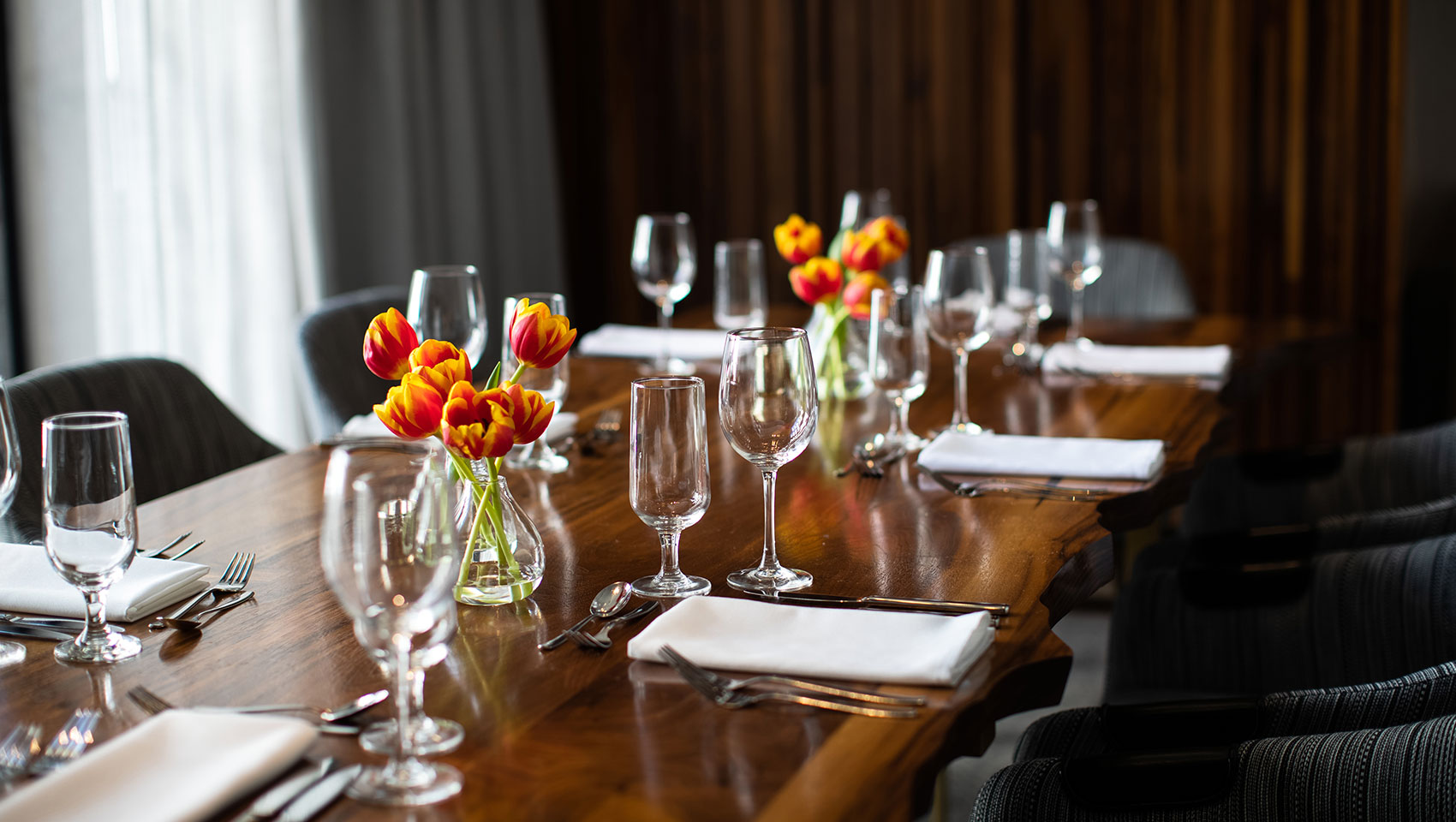 Private dining room set up in Calder room located in Kimpton Hotel Palomar Philadelphia glassware and floral arrangements in the center of a long wood table with chairs surrounding  