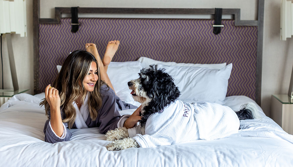 dog and owner wearing Palomar bathrobes laying on a guest room bed together