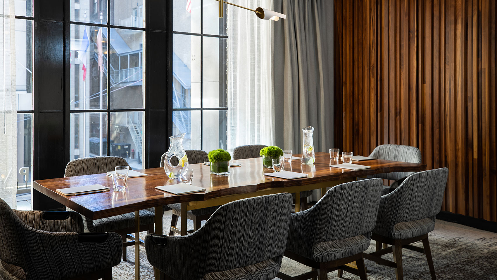 Boardroom Calder at Kimpton Hotel Palomar Philadelphia showing long, wood boardroom table with notepads and drinking glasses underneath a unique hanging fixture with horizontal lighting