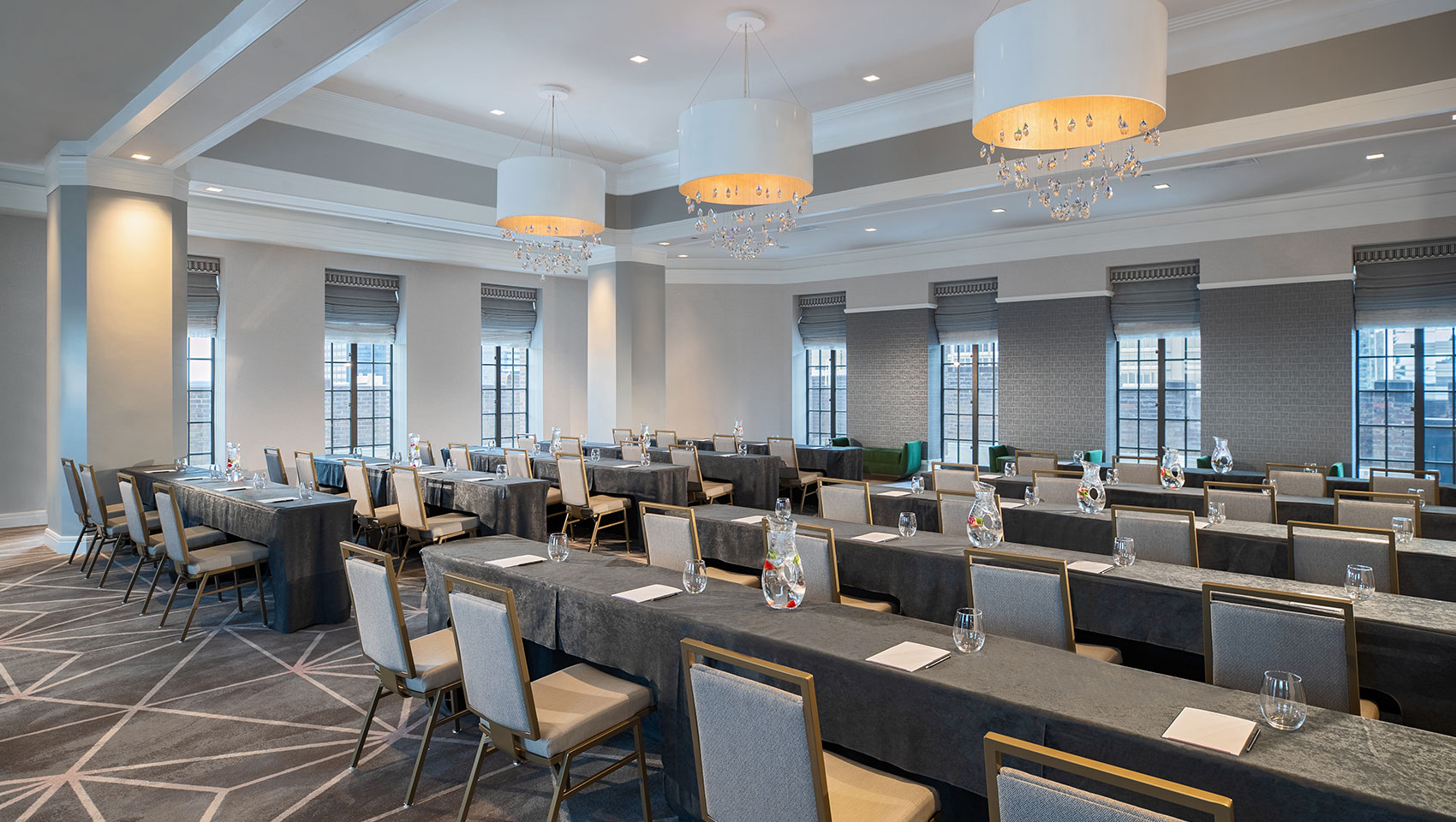 Classroom setup at Kimpton Hotel Palomar Philadelphia’s ballroom showing long tables with notepads all facing the same direction within a room surrounded with windows that overlook city views