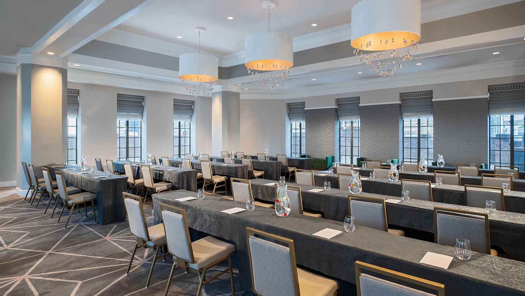 Classroom setup at Kimpton Hotel Palomar Philadelphia’s ballroom showing long tables with notepads all facing the same direction within a room surrounded with windows that overlook city views