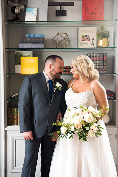 bride and groom standing in front of a bookshelf