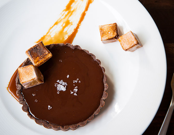 Chocolate dessert with toasted marshmallows on a plate next to a cup of coffee 