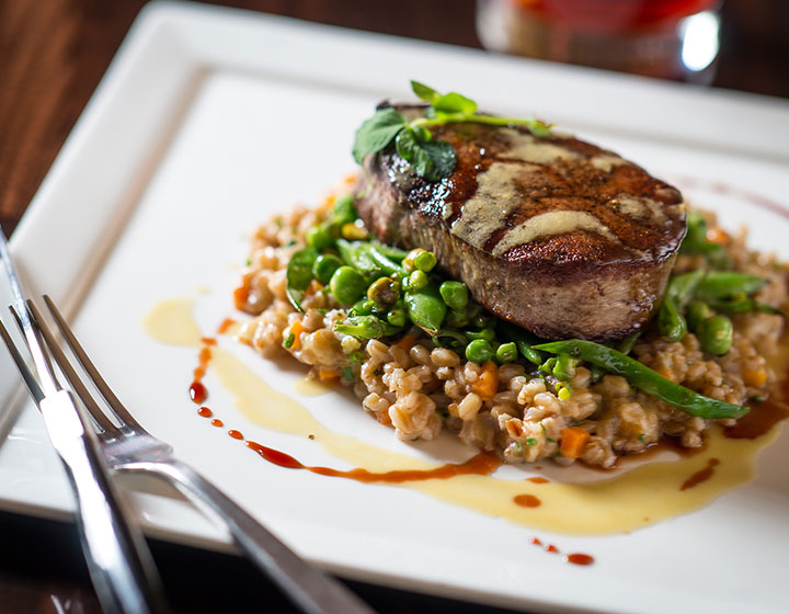 Filet pod with vegetables and a red wine reduction on a plate with a fork and knife