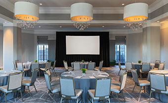 Kimpton Hotel Palomar Philadelphia ballroom with crescent round tables all situated behind a projector screen and underneath 3 identical, circular lighting fixtures