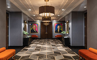Kimpton Hotel Palomar Philadelphia 24th floor meeting + event foyer area showing geometric carpet in open area, brightly colored plush seating, and a series of circular lighting fixtures